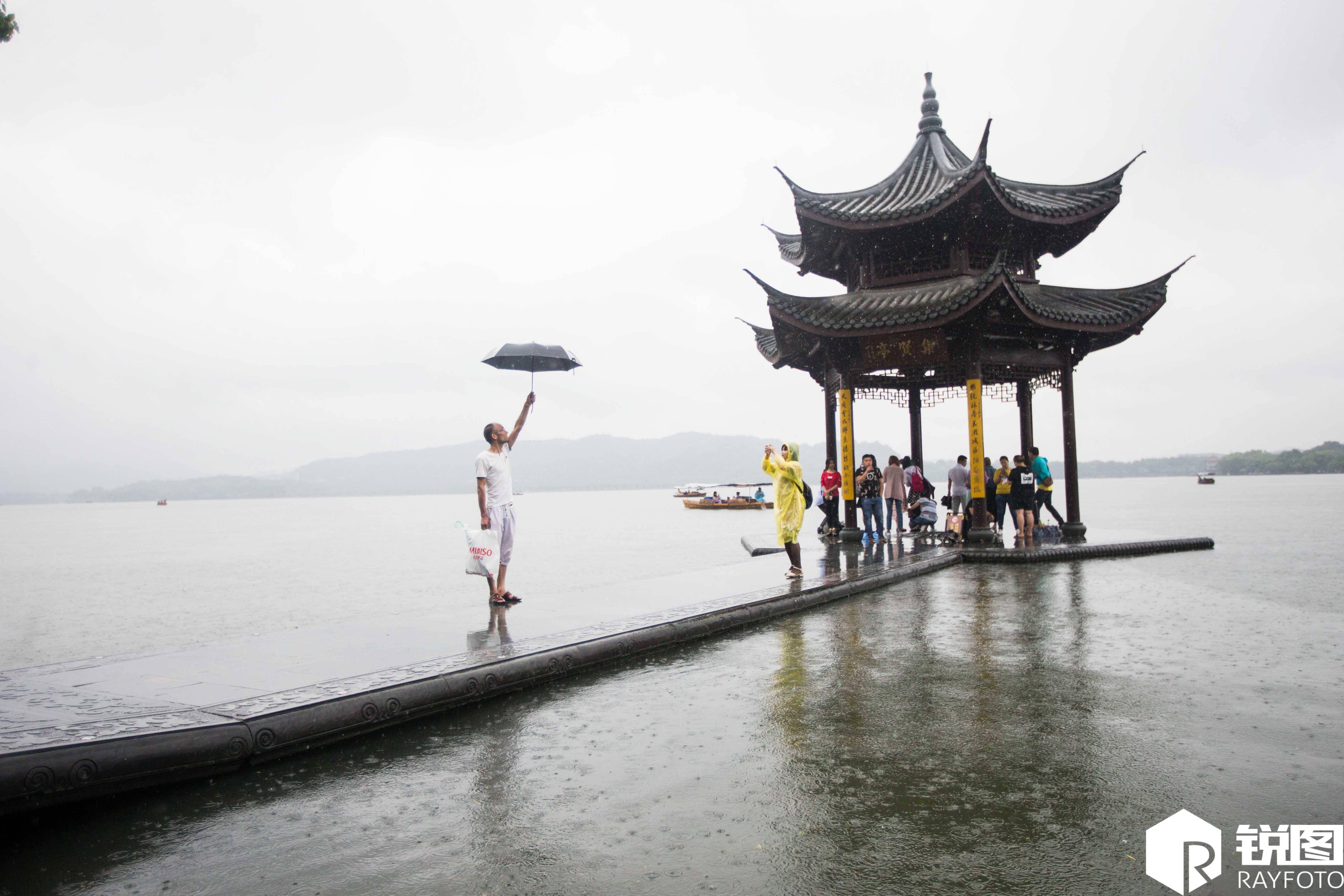 众多游客来到西湖边,在暴雨中摆pose拍照,一些游客为求更好的效果