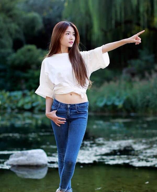 清澈的河水,倒映着蓝色紧身牛仔裤美女的身影,河边的绿色重重,景色
