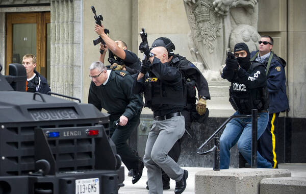 加拿大首都渥太华22日发生枪击案，一名可能持长枪的枪手在国家战争纪念碑附近打伤一名士兵，随后逃入联邦议会大厦，当地媒体报道，议会大厦内传出至少30声枪响。眼下议会大厦已封锁，加拿大首相哈珀已安全离开这一区域。警方正全力搜捕枪手。图为现场警方躲在车后掩护自己，和枪手发生枪战。