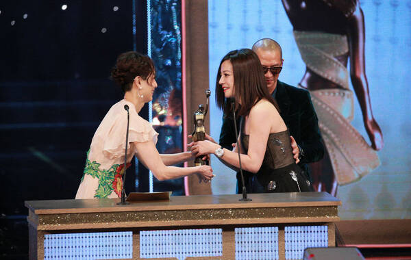 2015年4月19日，第34届香港电影金像奖颁奖典礼现场。刘青云、赵薇分获影帝后，许鞍华执导的《黄金时代》获得最佳影片、最佳导演、最佳摄影、最佳美术执导、最佳服装造型设计五项大奖，成为最大赢家。此外，歌手出身的王菀之凭借《金鸡SSS》中的妓女角色获得最佳女配角和最佳新演员，成为当晚另一大亮点。图为赵薇凭借《亲爱的》击败一众劲敌夺得影后，郑秀文为其颁奖，张家辉伸手轻抚赵薇的背部表示祝贺。