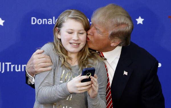 当地时间2016年1月16日，美国新罕布什尔州朴次茅斯，美国共和党总统参选人唐纳德-特朗普在当地举行竞选集会。图为特朗普在与一名支持者自拍合影时，亲吻这名女孩的脸颊。