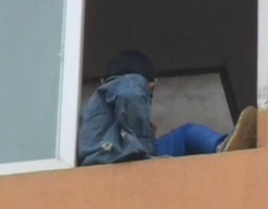 所幸救援人员游绳从天而降,一脚把男孩"踢"回房间内.