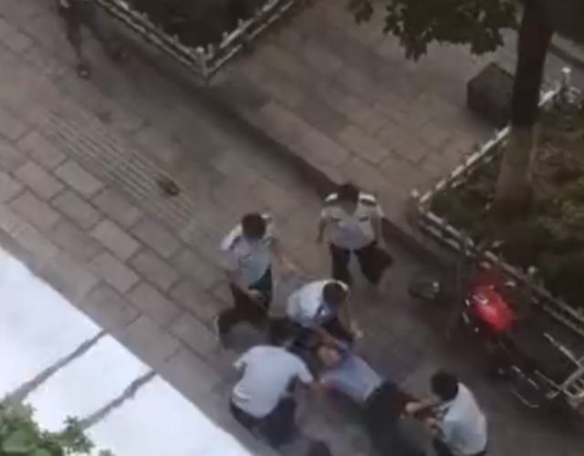 4名身穿城管制服的男子在街上拖着一名男子前行,过程中一人用手臂锁住
