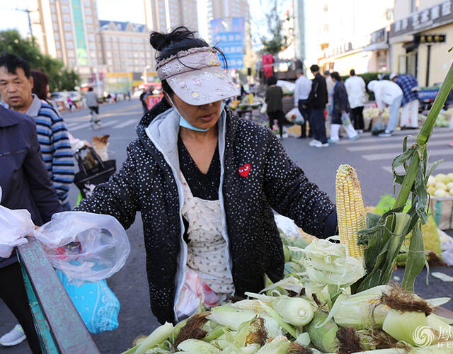 一位农家大姐穿着羽绒服正在卖水果玉米。