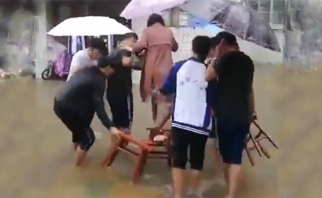 学生雨中持凳帮老师垫脚趟水