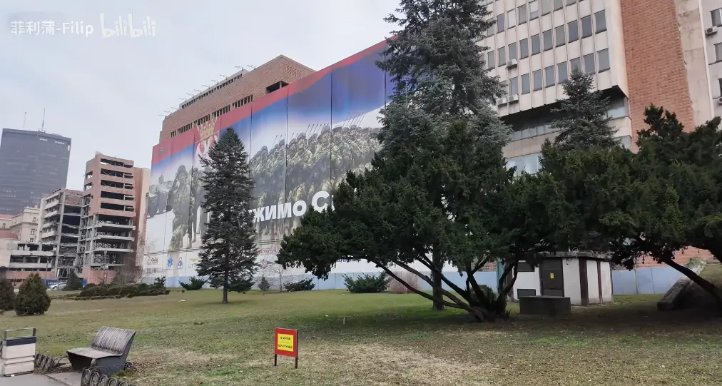 一块类似征兵广告的广告牌遮挡了被炸的大楼；据说美国希望塞尔维亚为了“美塞友好”考虑，遮一遮残骸。