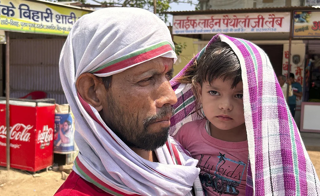 当地时间2023年6月17日，印度拉利特普尔，男子给孩子身上盖上围巾遮挡酷暑。