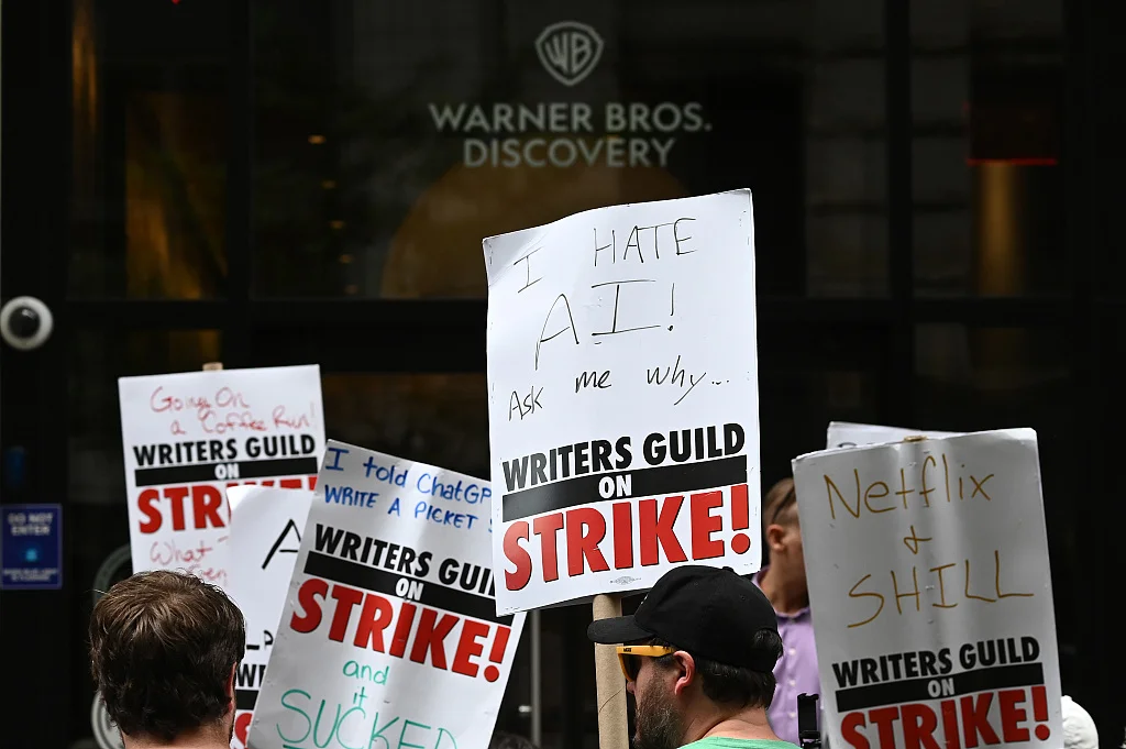 当地时间2023年7月13日，美国纽约，美国东部编剧协会成员手持标语，与美国演员工会成员一起在华纳兄弟的公司外抗议。