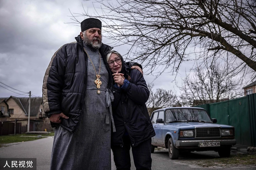 当地时间2022年4月12日，乌克兰基辅州Gostomel村，牧师与一名死者的亲属。人民视觉 图