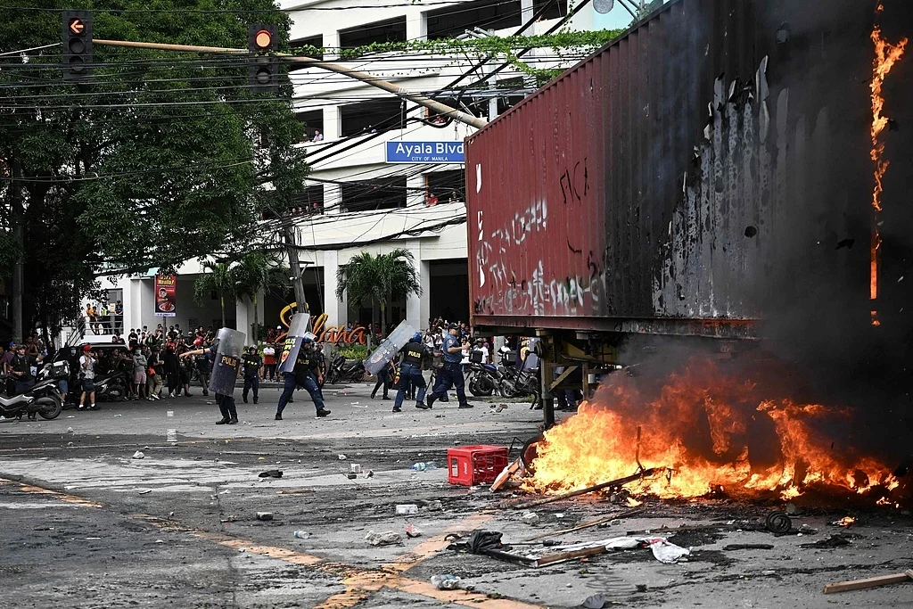 21日，菲律宾全国爆发反腐抗议活动。图为一群青年焚烧拖车后向警察投掷石块，警察举盾牌防御。（视觉中国）