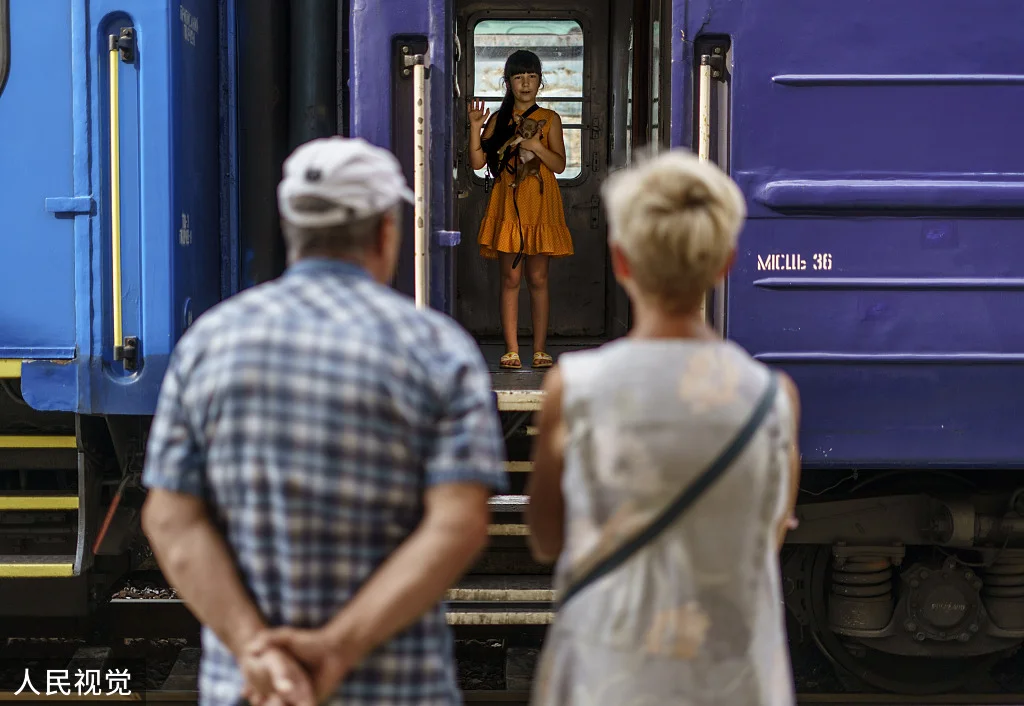 当地时间2022年8月2日，顿涅茨克地区波克罗夫斯克，在疏散列车上，一名小女孩抱着她的狗，向她的祖父母挥手告别。政府发布命令，要求居民离开顿涅茨克地区，因为他们正在为秋冬做准备，并担心那里的许多人可能没有暖气、电，甚至清洁的水。人民视觉 图