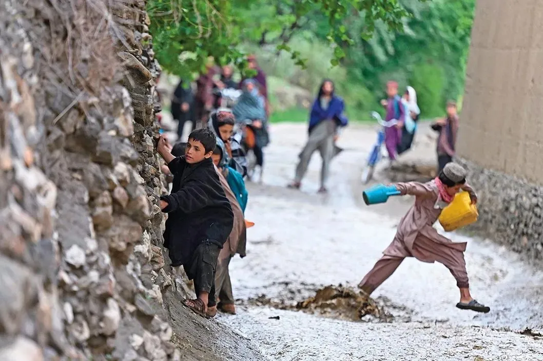 5月29日，在阿富汗瓦尔达克省迈丹城赛义达巴德，孩子们走在雨后泥泞的街道上 新华社/法新
