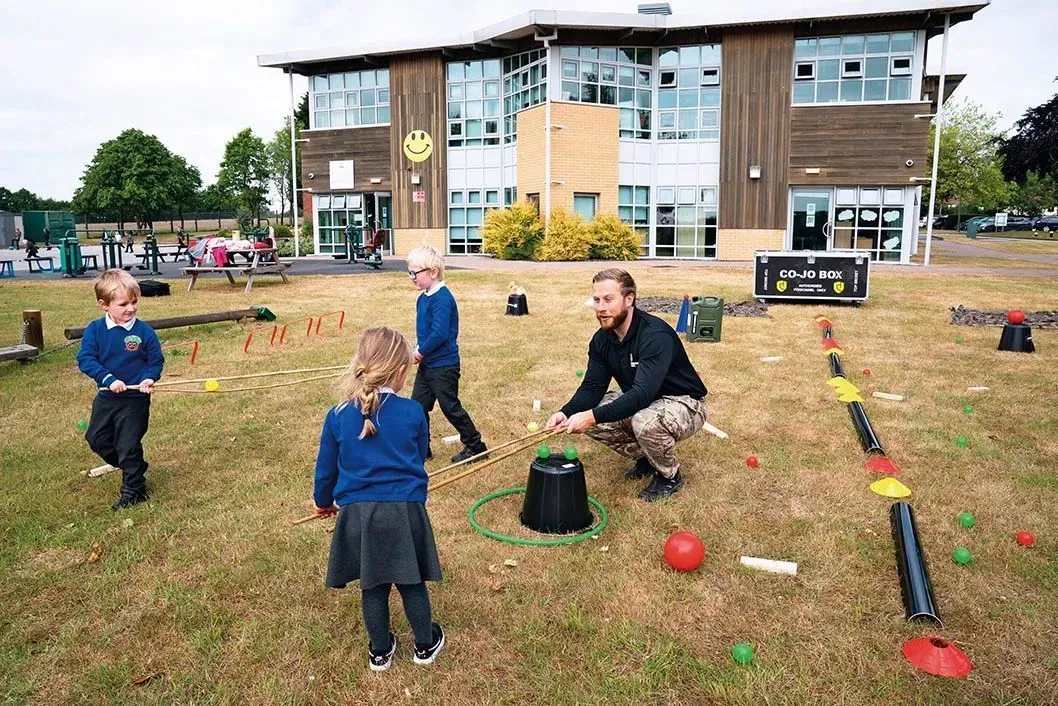2020 年 6 月 8 日，在英国斯塔福德郡，兰迪伍德小学学前班的学生们在培训老师斯图·威尔金森(右一)的带领下用小棍子做保持安全距离相关游戏 新华社发(乔恩·休珀摄)