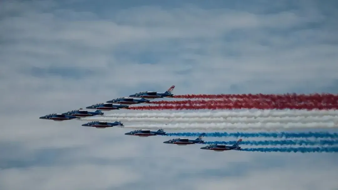 ▲ 飞行编队接受检阅时，打头阵的是法兰西巡逻兵飞行表演队（Patrouille de France）的9架阿尔法教练机（Alpha Jet），飞行中尾部喷洒出蓝白红法国国旗三色烟雾。（法新社图）