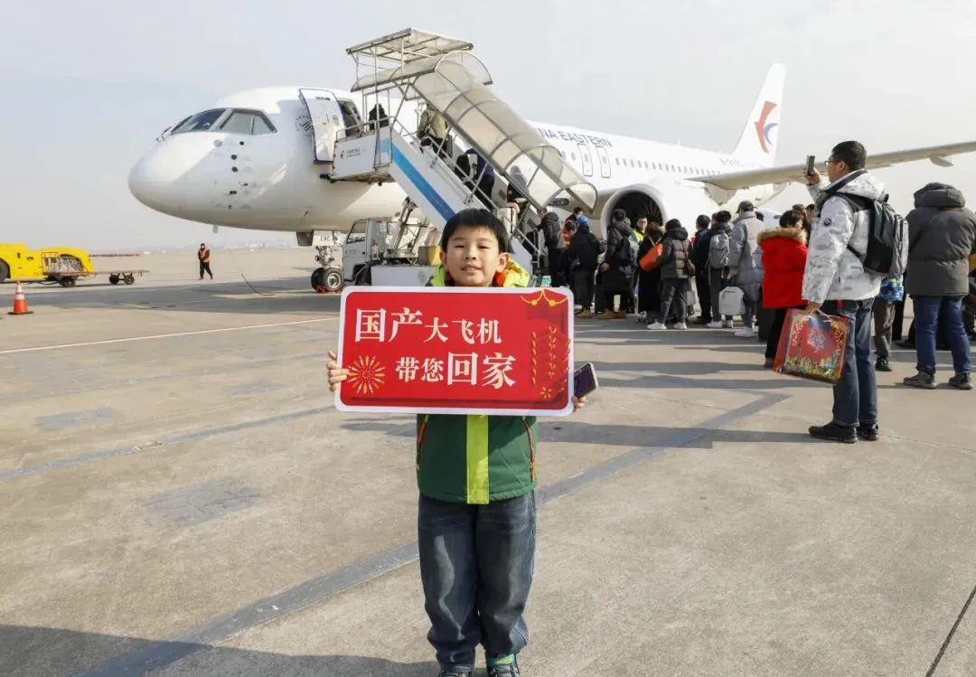 ▲1月26日，在上海虹桥机场，一位小旅客手举标语牌在国产大型客机C919前合影。（新华社）
