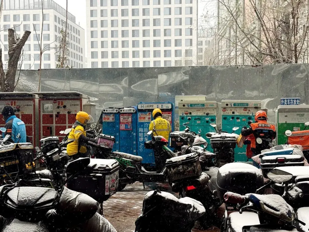 12月12日,下雪的北京,丰台区丰科万达商圈附近电动车停车场、换电站出现拥堵,骑手忙碌地取、送订单,或者边休整边等待订单。 摄影/本刊记者 王诗涵