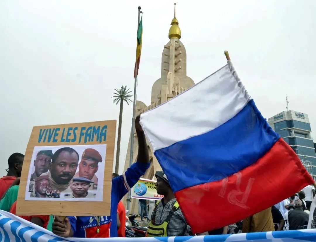 2021年5月28日，在马里首都巴马科举行的马里武装部队（FAMA）示威活动中，马里人手持一张印有马里军政府领导人阿西米·戈伊塔（Assimi Goita）形象的照片和俄罗斯国旗。图源：Amadou Keita/路透社