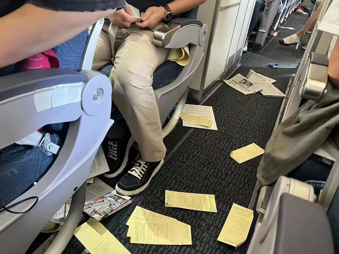 机舱里小学生的书包飞起来，里面的卷子散落一地。