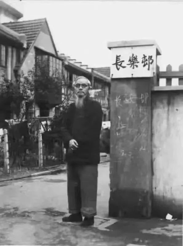 丰子恺在长乐村弄口。“长乐村”三个字为丰子恺所书，他身后的尖顶楼房为“日月楼”。