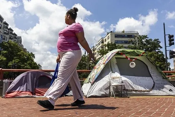一名行人走过华盛顿环岛无家可归者的帐篷。美国总统特朗普在白宫新闻发布会上宣布，将在华盛顿特区部署国民警卫队，声称该地区的犯罪“失控”，誓言要清除首都的无家可归者营地。