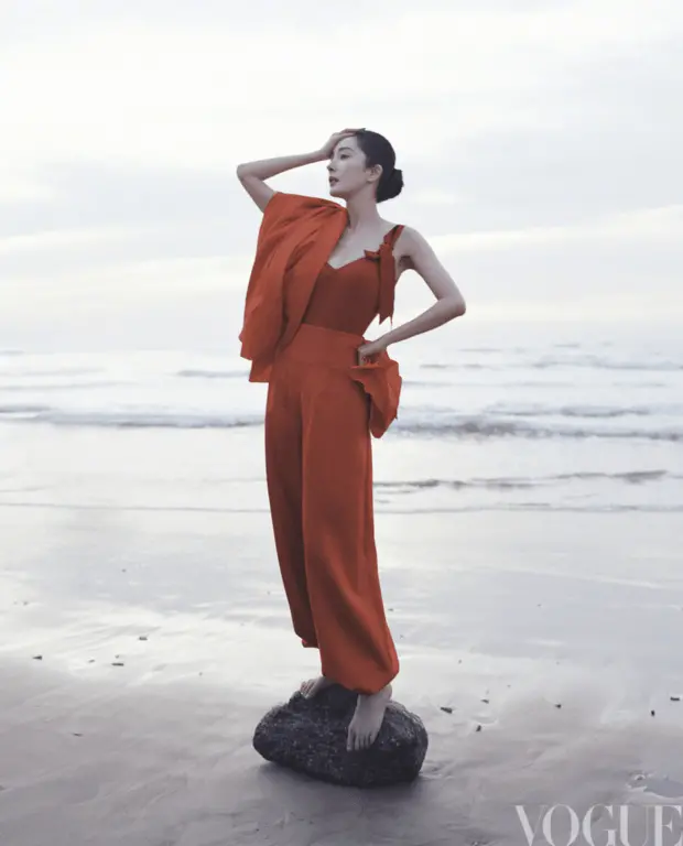 杨幂身着红装立于海边,抬手轻抵脖颈的姿态利落明艳。