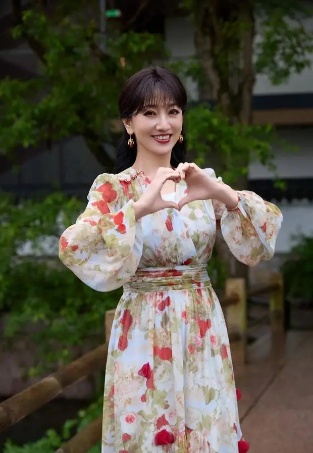 赵雅芝穿着碎花裙比心，绽放灿烂笑容，十分明媚动人。