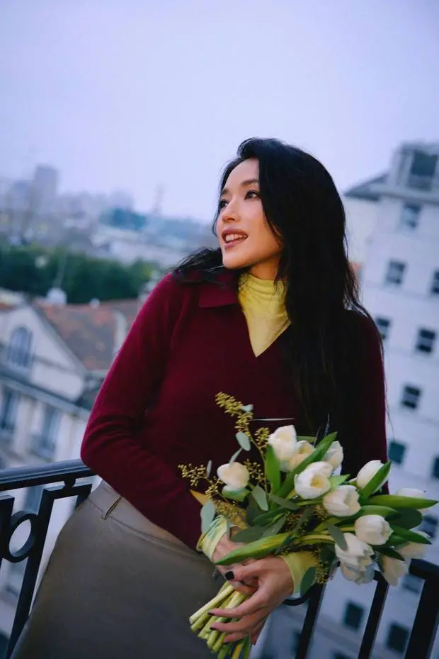 搜狐娱乐讯 近日，一组舒淇美图释出。图中，她身着酒红针织衫，手捧白色郁金香花束，在城市阳台侧头浅笑。