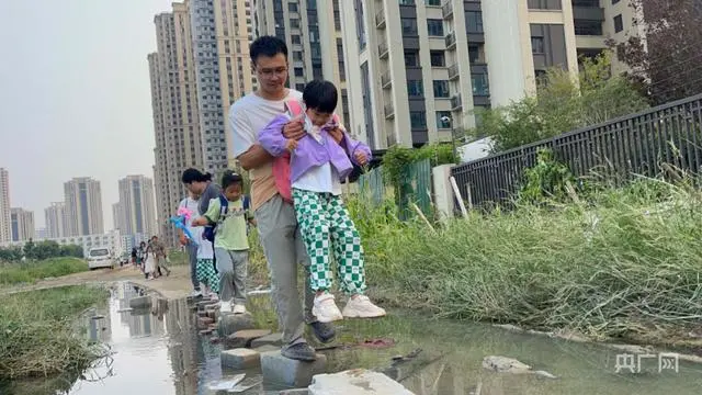 正值放学时间，家长们带领孩子小心翼翼脚踩砖头通过此积水路段（央广网见习记者 张丽娜 摄）