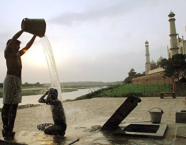 一个印度青年在别人帮助下冲澡,刚打上来的水温度很低,青年冻得打了一