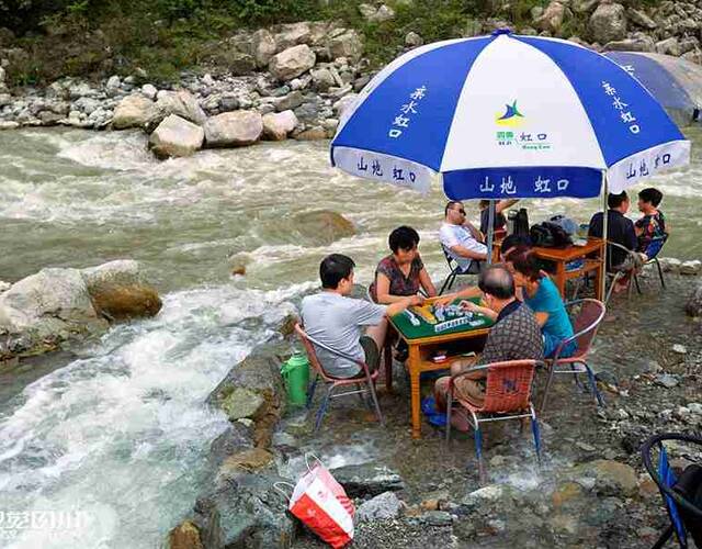 找块地摆个麻将局,在蓝白大伞下,游客们双足泡水,惬意搓麻,寄情山水间