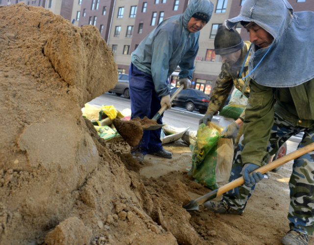 在现场,只见一名力工用手撑起编织袋,老陶和另一位工友用铁锹将沙子铲