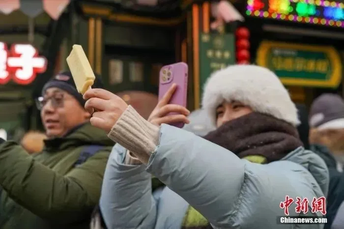 1月2日,在黑龙江哈尔滨中央大街,游客身着厚衣服在寒冷的天气中品尝雪糕,手拿雪糕拍照,成为哈尔滨冬日一景。图为游客拍摄雪糕。中新社发 赵宇航 摄