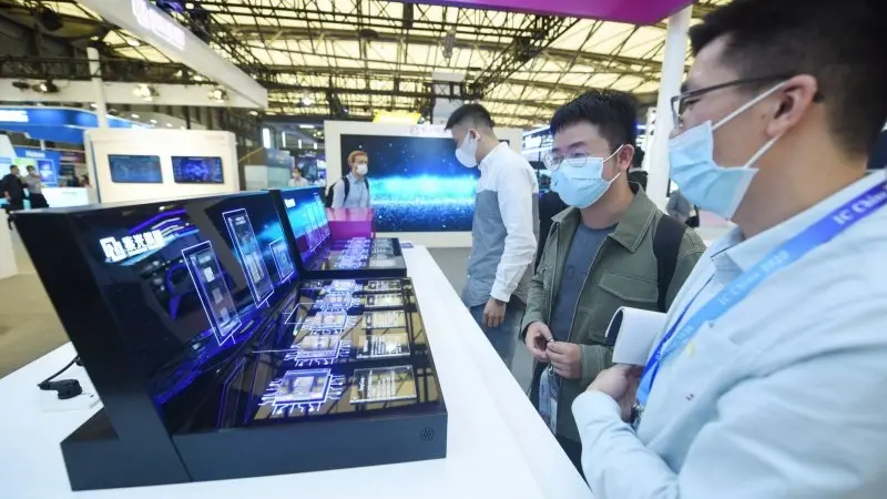 图/参观者在中国上海举行的第18届中国国际半导体博览会上观看不同展位展出的各种芯片