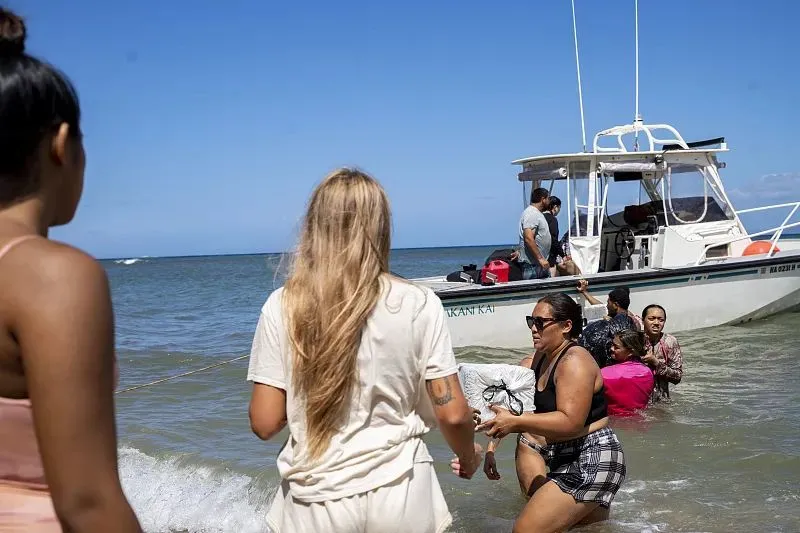 8月11日，美国夏威夷，数十名卡哈纳当地居民排队进入水中，帮助将物资传递到岸上。图源：视觉中国