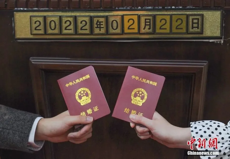 资料图：2022年2月22日，浙江杭州，一对新人拿结婚证和日期数字拍照。 中新社记者 王刚 摄