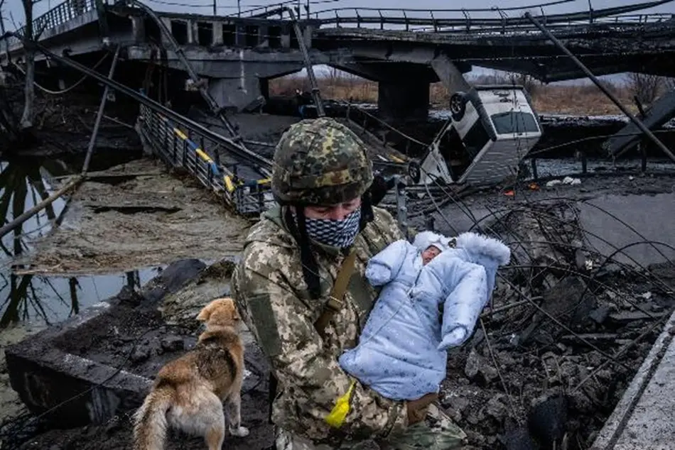 一名乌克兰士兵抱着一个婴儿穿过基辅郊区一座被毁的桥梁。 图源： CNN